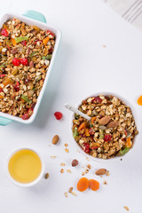 Baked granola in the baking tray  and  white ceramic bowl with various delicious ingredients for healthy breakfast