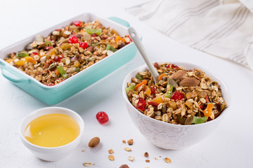 Baked granola in the baking tray  and  white ceramic bowl with various delicious ingredients for healthy breakfast