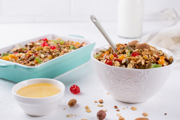 Baked granola in the baking tray  and  white ceramic bowl with various delicious ingredients for healthy breakfast