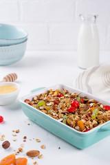 Baked granola in the baking tray  and  white ceramic bowl with various delicious ingredients for healthy breakfast