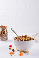 Healthy breakfast concept. Baked granola in white ceramic bowl and glass jar on the kitchen table.