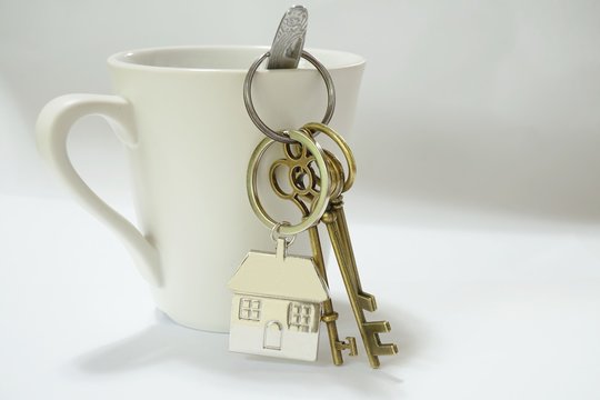 Home keys with house keyring hanging on white coffee cup
