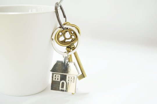 Home keys with house keyring hanging on white coffee cup