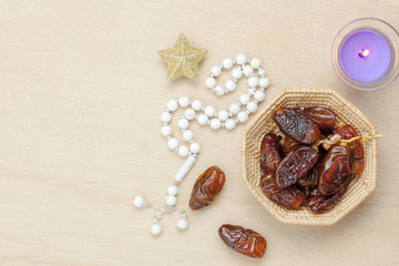 Table top view aerial image of decoration Ramadan Kareem holiday background.Flat lay date in wood basket with white rosary & aromatherapy candle .Essential object star on rustic wooden at office desk.