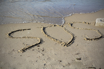 SOS - word drawn on the sand beach with the soft wave