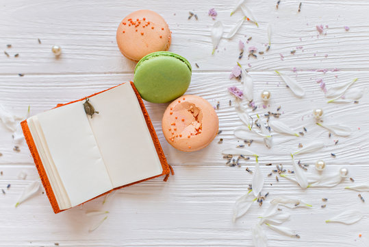 A flat lay of a colorful macarons , notebook for records on the white texture background