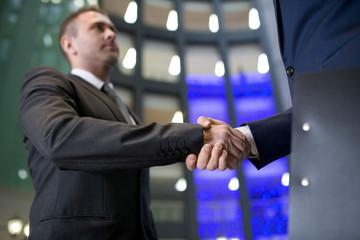 Close-up of serious confident businessman making handshake with new business partner in office hall