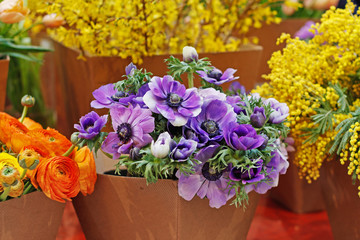 Bouquets of beautiful anemone, ranunculus and mimosa flowers in paper flower pots at market