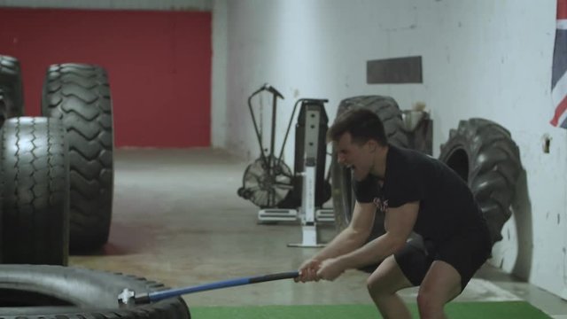 Slow motion action shot of a young MMA fighter hitting a tractor tire with a sledgehammer in a gym