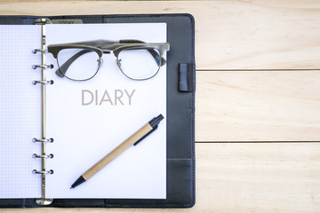Diary with eyeglass and pen on the wooden table, for writer concept