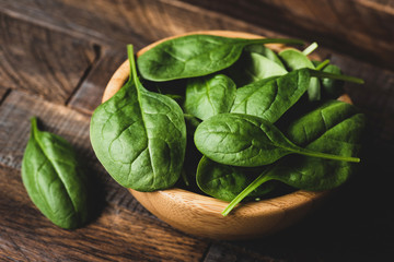 Baby spinach in wooden bowl, closeup view selective focus. Dieting, healthy eating, healthy lifestyle, fitness, weight loss concept