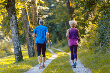 Full length rear view of a senior couple wearing cool running outfits while jogging together outdoors on an idyllic path in the park in summer 