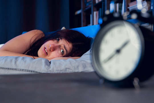 Picture of dissatisfied woman with insomnia lying on bed next to alarm clock at night