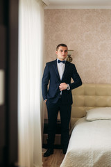 Handsome groom on a wedding day stand near the window