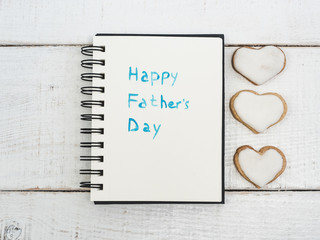 Glazed heart shaped cookies, sketchbook with handwritten congratulation on Father's day on a beautiful, white table. Top view. Happy family concept