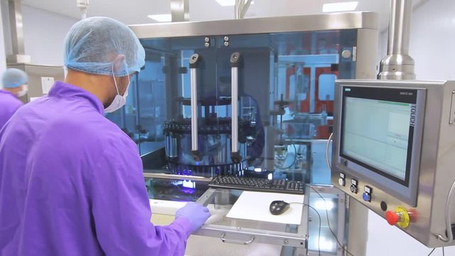 Operator control pharmaceutical manufacturing equipment. Factory worker using touch screen to control manufacturing line. Control panel of automated production line at pharma factory