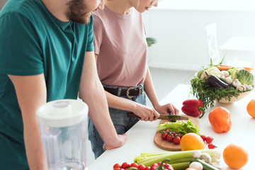 Obraz na płótnie Canvas cropped image of vegan girlfriend cutting vegetables at kitchen
