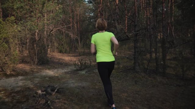 woman in a sports outfit runs through a beautiful summer forest