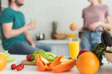 cropped image of vegan couple talking in kitchen with fruits and vegetables on foreground