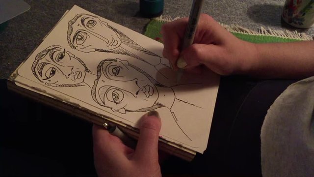 Medium close up of artist's hands drawing sketches in pen and ink on a notepad