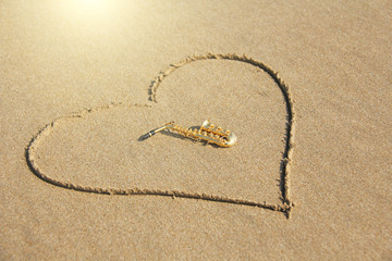 The golden alto saxophone lies inside the heart of the sand, on the beach. Romantic musical...