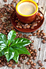 Cup of coffee with fresh coffee leaves on coffee beans background