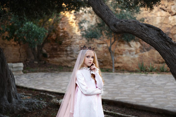 charming whute witch foreteller stands in a mysterious magical forest in a wedding dress with a veil and crown