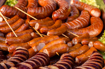 assorted sausages grilled on skewers on a large plate, mushrooms on the grill. Street festival food.