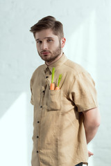 portrait of bearded man with fresh carrots in pocket, vegan lifestyle concept
