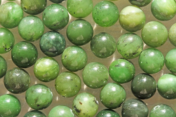 Natural green jade nephrite mineral stones beads. Green and grassy natural background made of round...