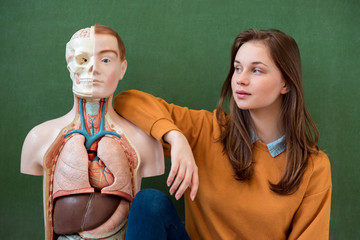 Cool female high school student portrait with an artificial human body model. Student having fun in...