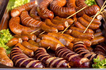 assorted sausages grilled on skewers on a large plate, mushrooms on the grill. Street festival food.