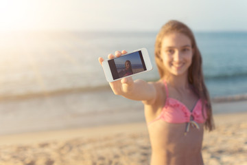Young woman taking selfie at the sandy beach with the sea and horizon in the background on hot summer day travel and tourism concept