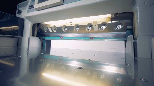 A man is putting four stacks of paper under a cutter which shears its sides