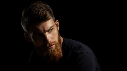 Portrait of young handsome bearded man looking forward Studio shot over black background.