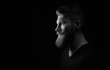 Dramatic concept Black and white close-up portrait of young handsome bearded man looking forward. Studio shot on black background