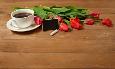 tulips are on wooden boards, cup of coffee with small chalkboard, greeting concept in retro style
