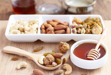 Dried fruits and variety of nuts into a dish and bowl of honey on the wooden background.