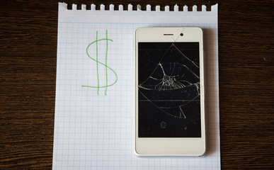smartphone with a broken screen on a paper sheet with the inscription dollars. Saving