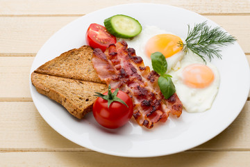 Fried eggs with bacon on the wooden table.