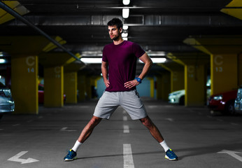 Young male runner stretching his muscles before workout in the underground car parking.