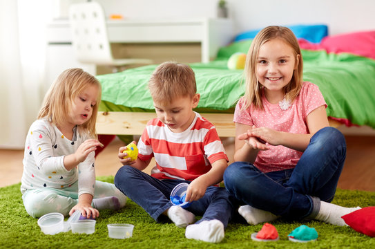 childhood, leisure and people concept - group of kids with modelling clay or slimes at home