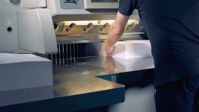 An employee is adjusting two large piles of paper under a cutter which ploughs them in four parts 