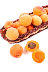 Naklejka na ściany i meble Several of harvested apricots in basket with whole and halved apricots on white background..