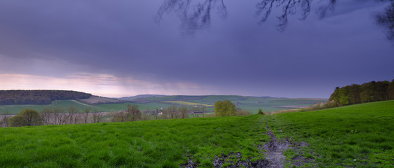 Spring storm clouds and rain over Butser Hill viewed from Old Winchester Hill near West Meon, South Downs, Hamspshire, UK