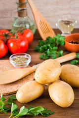 Raw potatoes in the peel, vegetables, greens and spices for cooking a dish on a wooden table