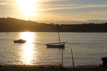 Atardecer sobre un puerto pesquero con barcos de fondo y la luz del sol poniéndose en el horizonte