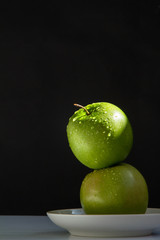 two juicy green Apple clean are to each other on a white saucer on the table.Low key