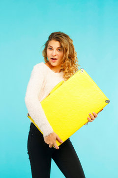 Young happy beautiful woman holding yellow suitcase over blue background