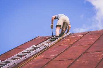 A man is repairing a roof standing on the stairs